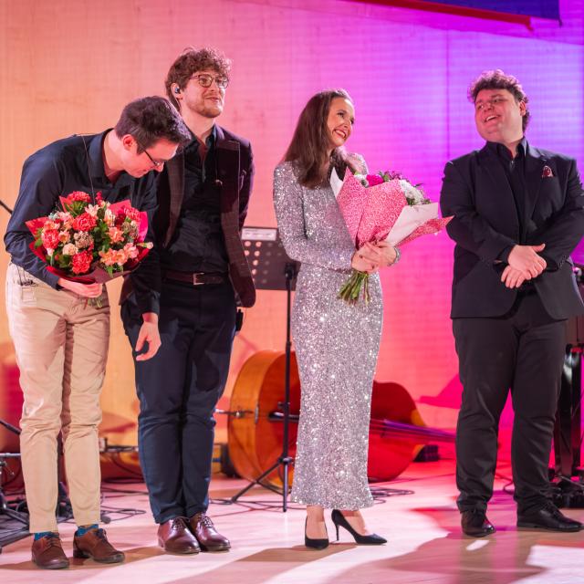 Finał koncertu: wokalistka trzyma bukiet i śpiewa na scenie, za nią kontrabasista Piotr Cienkowski, po lewej perkusista Jan Garstecki, po prawej pianista Julian Kokociński przy fortepianie.